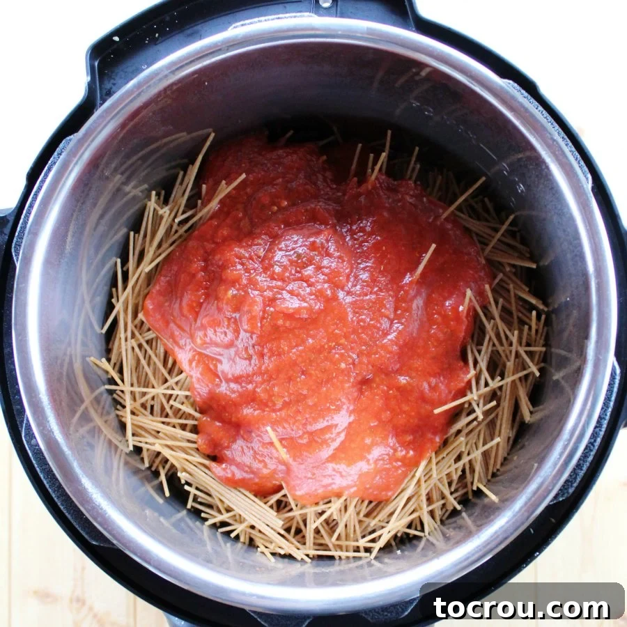 Instant Pot Magic: Creamy One-Pot Meatball Spaghetti 2 Uncooked spaghetti noodles layered in an Instant Pot, topped with rich tomato sauce, ready for pressure cooking.