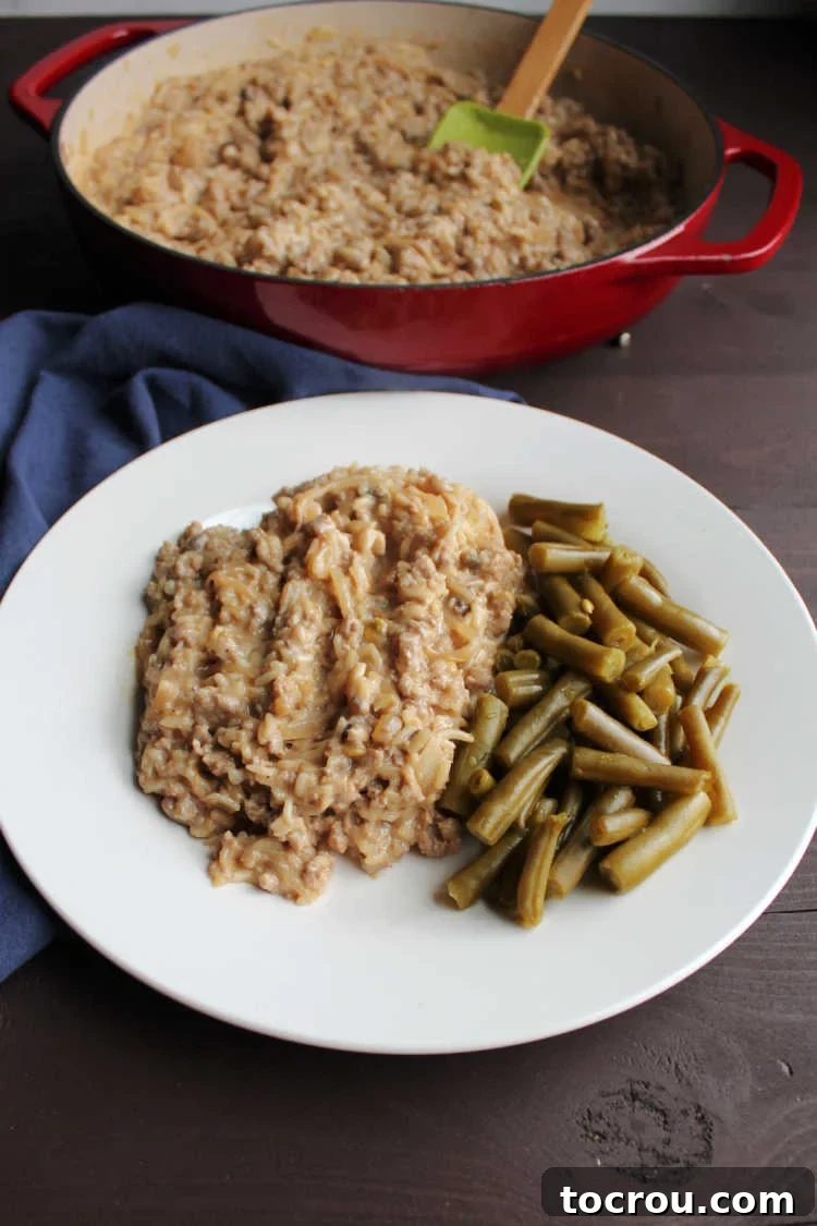 A close-up of a single serving of creamy ground pork and rice, with a blurred skillet of the remaining dinner in the background, inviting diners to enjoy this comforting dish.