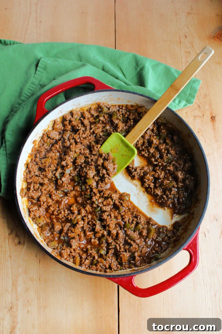 Sloppy Joe Mixture in Skillet Enameled cast iron skillet filled with simmering ground beef coated in a thick, rich cola-infused tomato sauce, ready to be served.