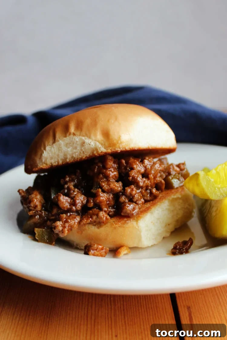 Sloppy Joe with Pickles Close-up of a toasted bun piled high with coca-cola sloppy joe mixture, served on a plate with two pickle spears.