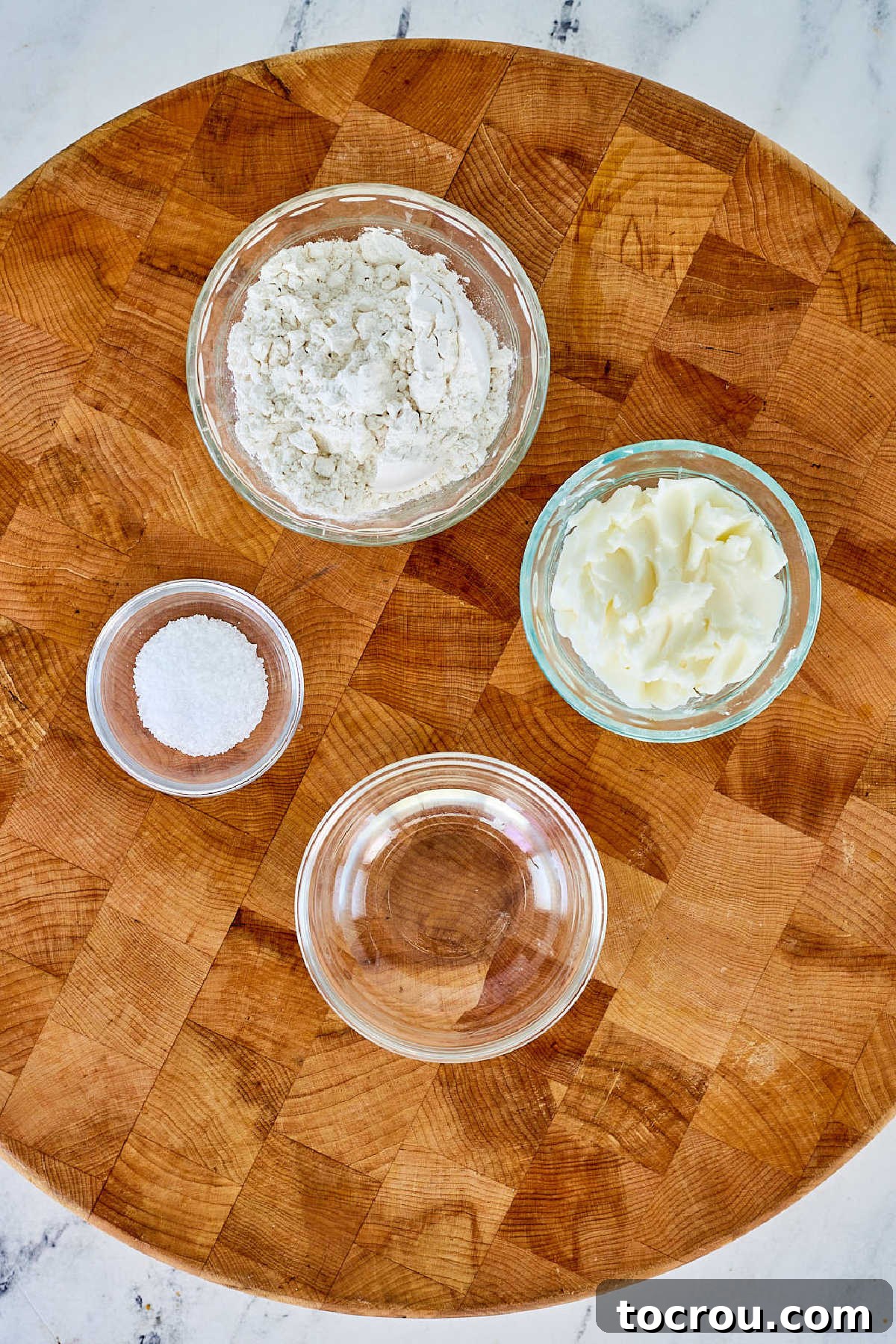 Essential ingredients for an exceptional pie crust laid out: pristine white flour, a sprinkling of salt, a generous block of solid lard, and a bowl of ice-cold water, all awaiting transformation into pastry.