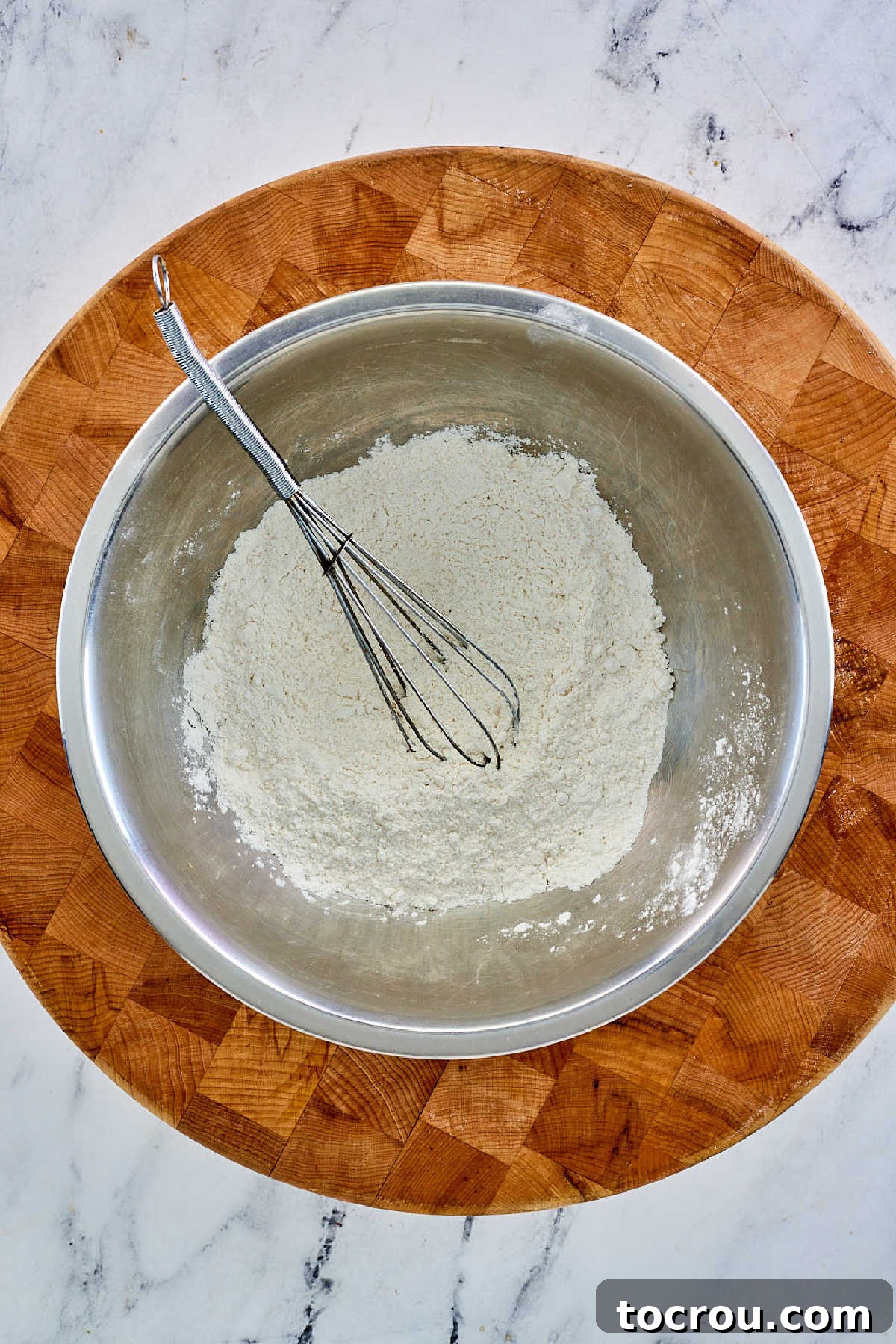 A pristine white mixing bowl containing a mound of all-purpose flour and a dash of salt, poised for the next step in pie crust preparation.