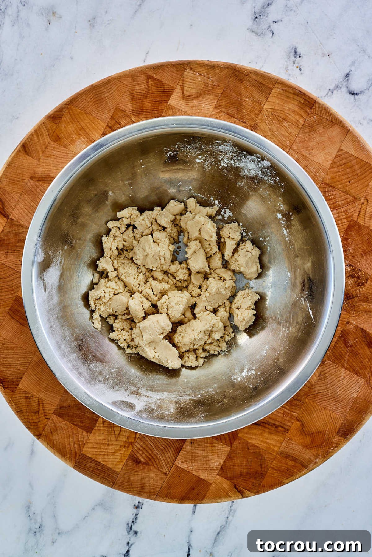 The initial stage of pie crust dough formation: a mixing bowl holds flour with pieces of cold lard cut in, forming a coarse, crumbly mixture before water is added.