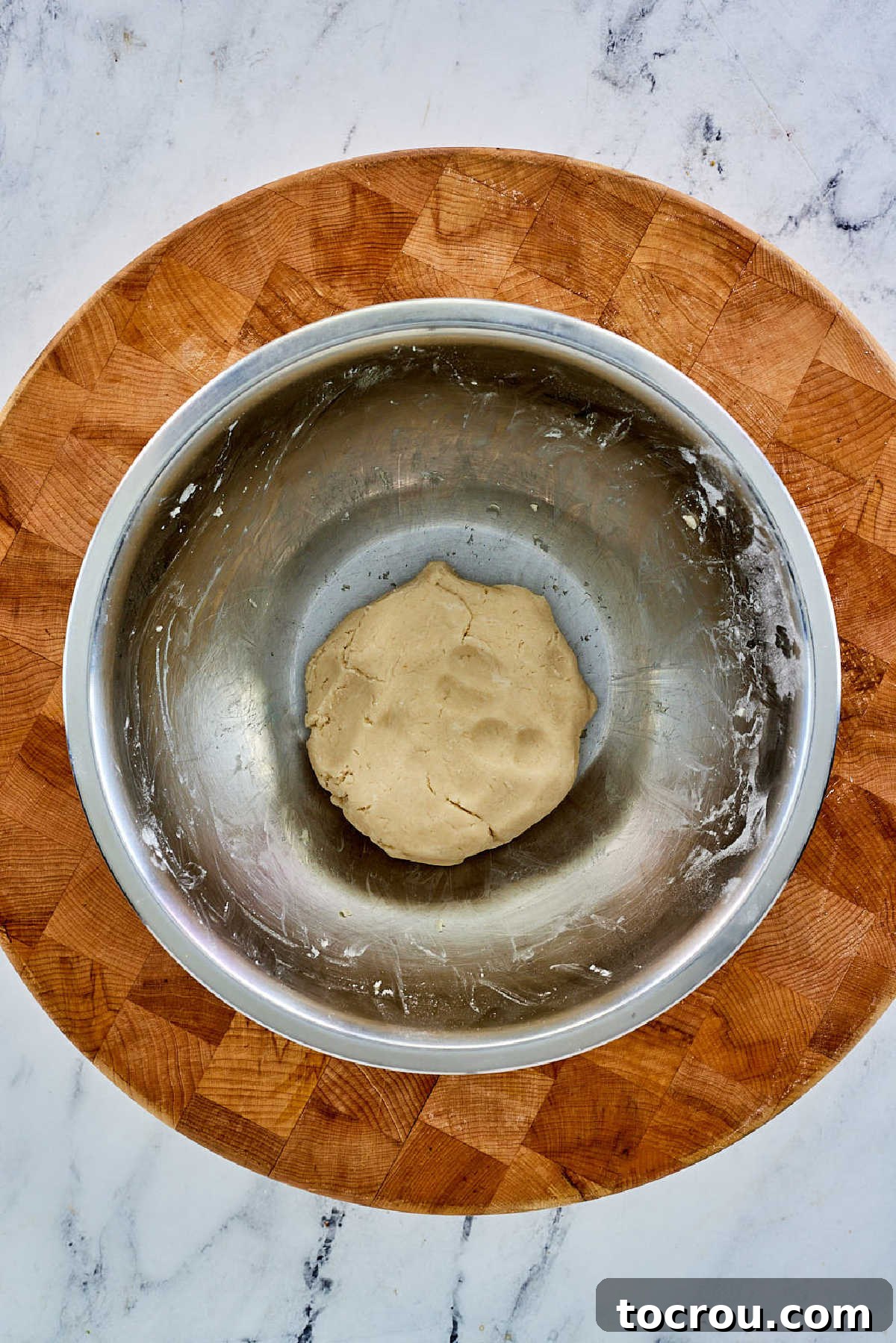The pie crust dough has come together, forming a cohesive ball in the mixing bowl after the precise addition of ice-cold water, ready for chilling.