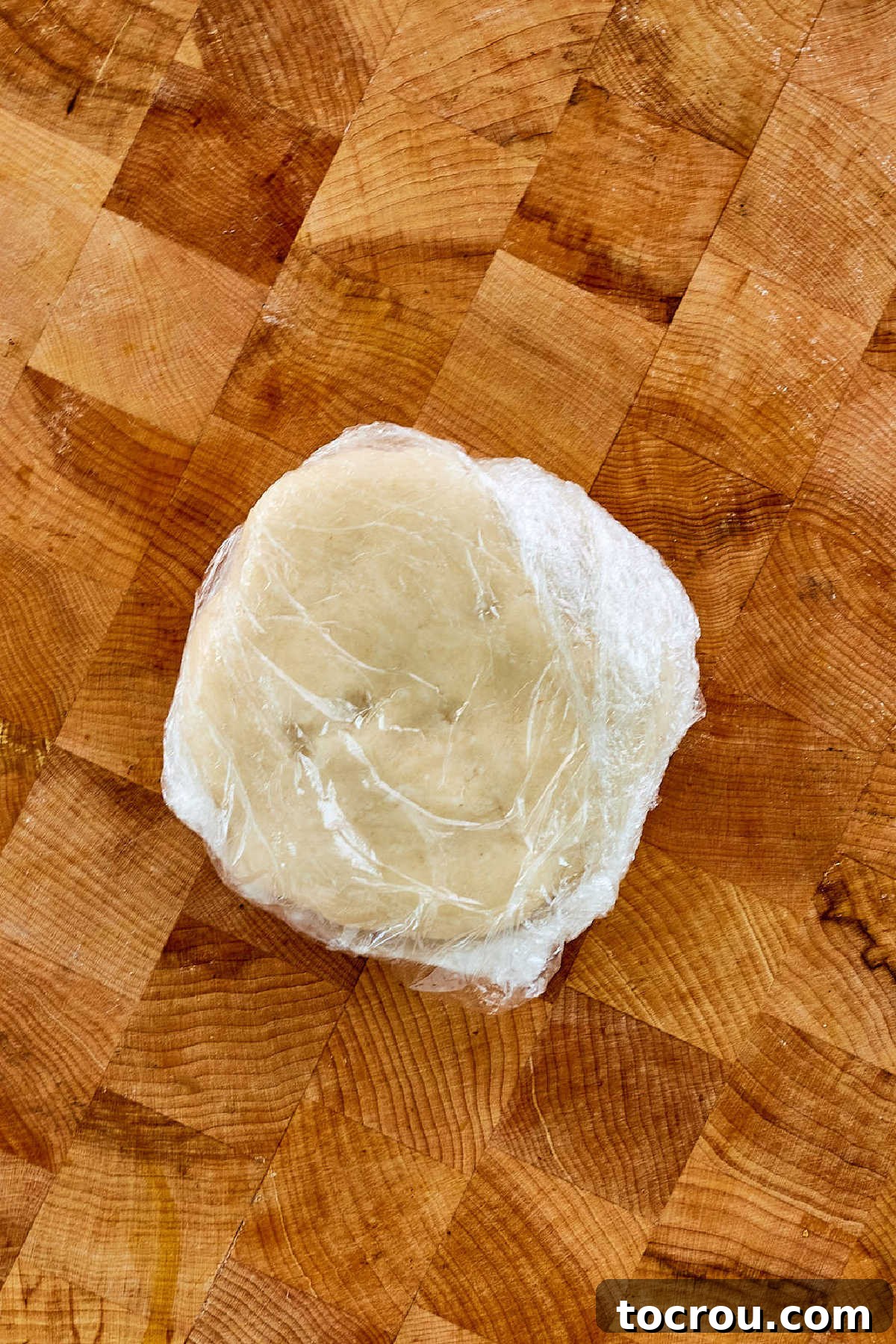 A freshly prepared lard pie crust pastry disk, securely wrapped in clear plastic film, is ready to be placed in the refrigerator for chilling.