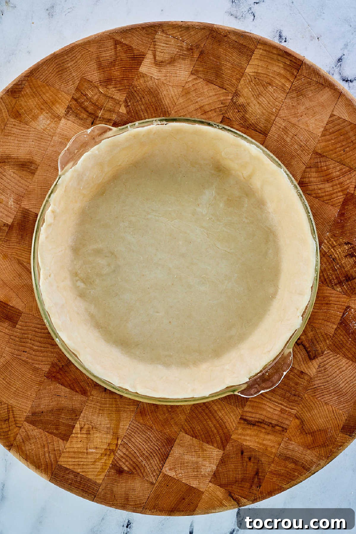 The delicate lard pie crust pastry, now neatly fitted into a clear glass pie plate, its edges meticulously crimped and prepared for filling.