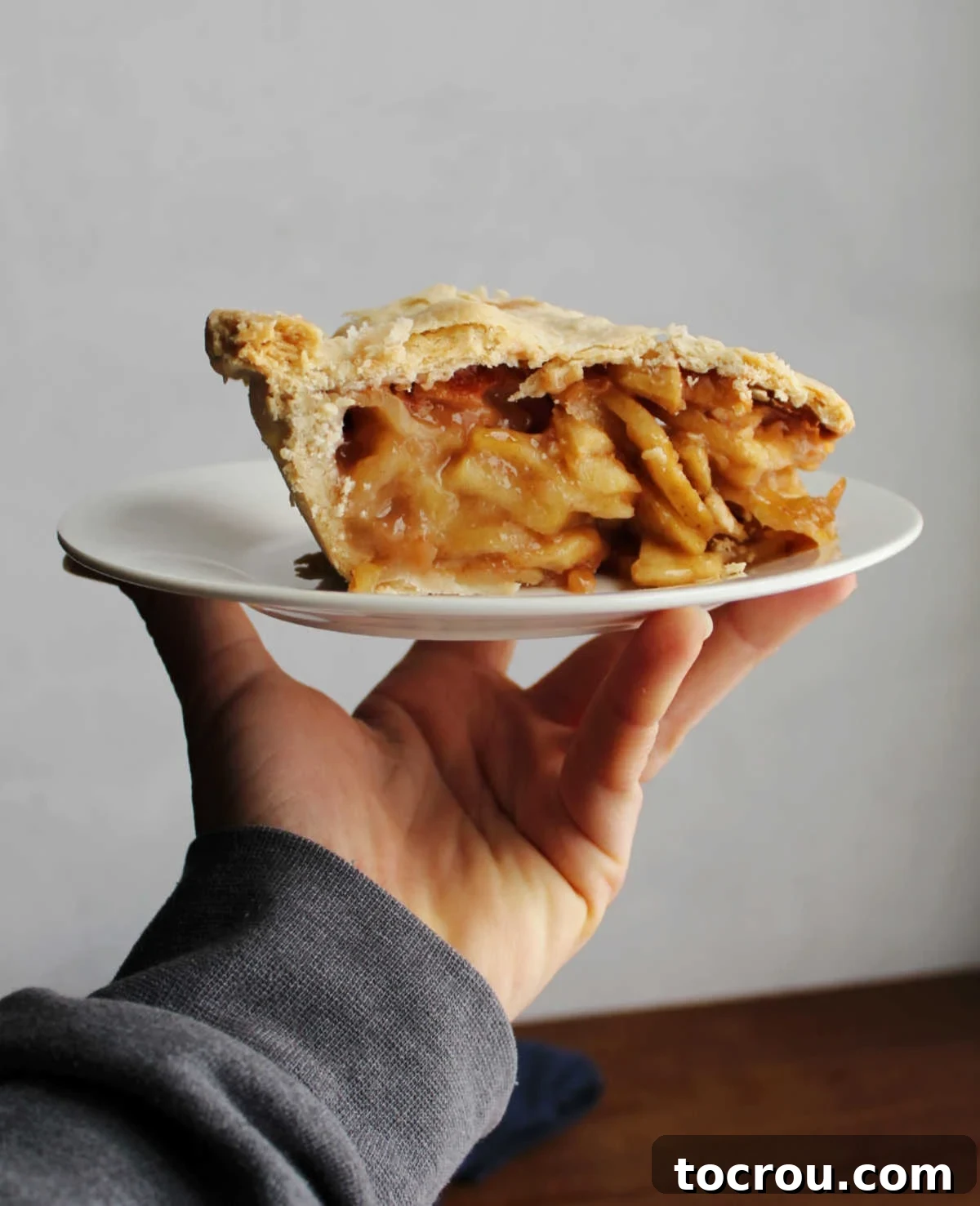 A hand gently holding a plate featuring a perfectly baked slice of apple pie, ready to be enjoyed.