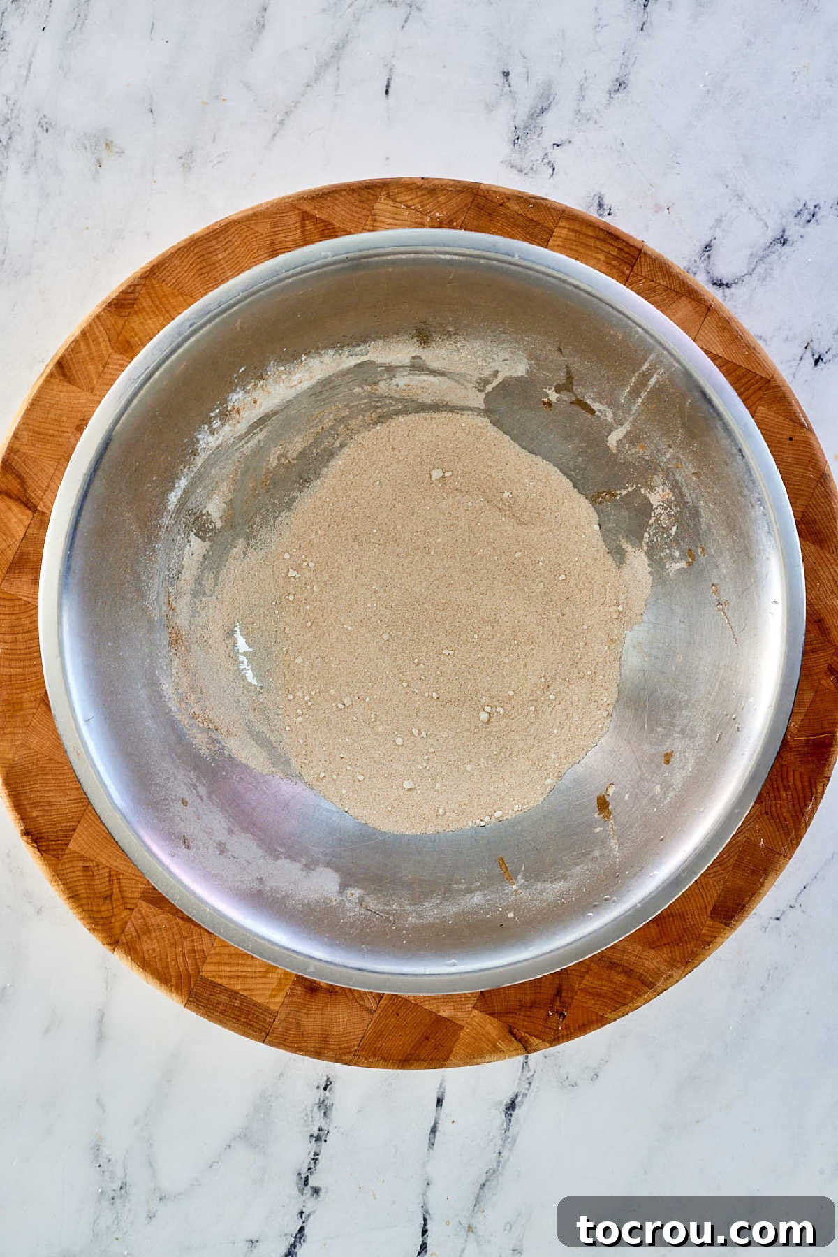 A mixing bowl filled with a dry mixture of cinnamon, flour, and sugar, prepared for tossing with apple slices.