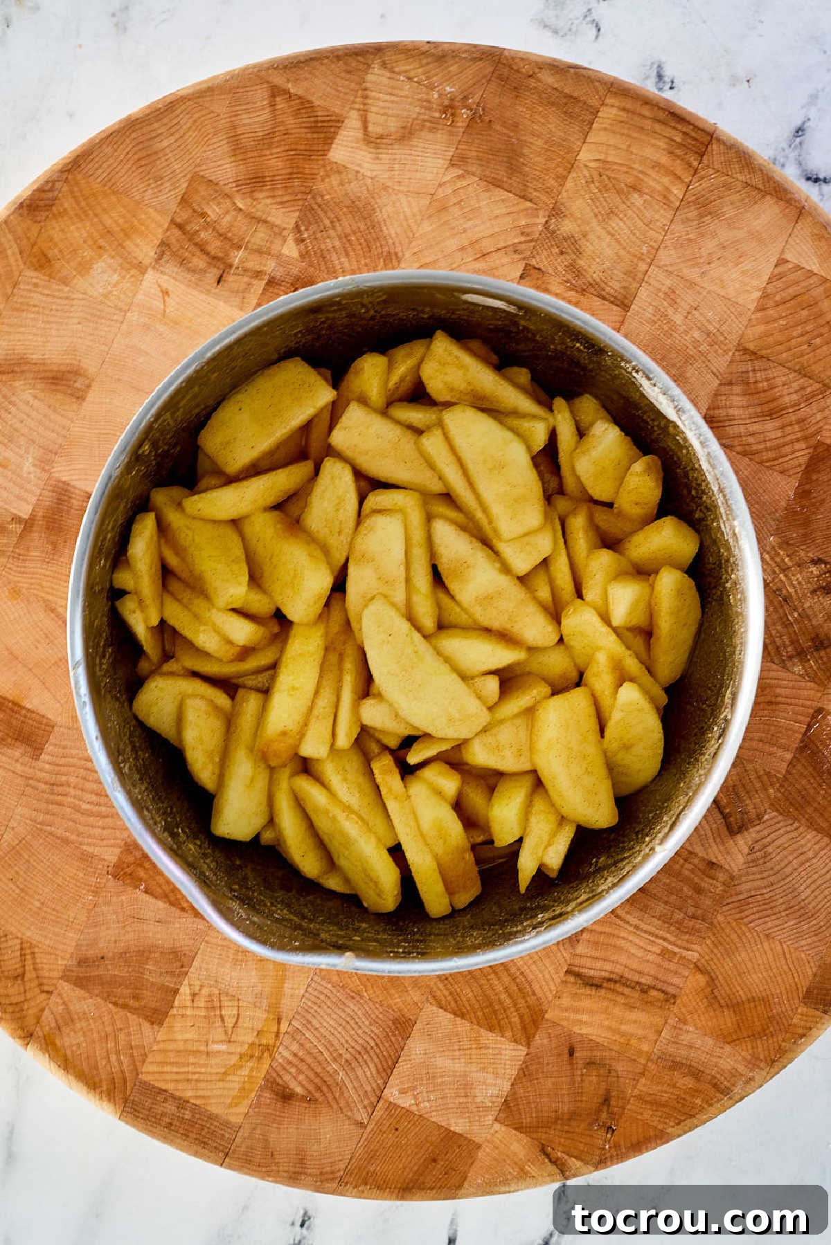 Peeled apple slices generously coated in the cinnamon-sugar mixture within a mixing bowl, ready for the pie crust.