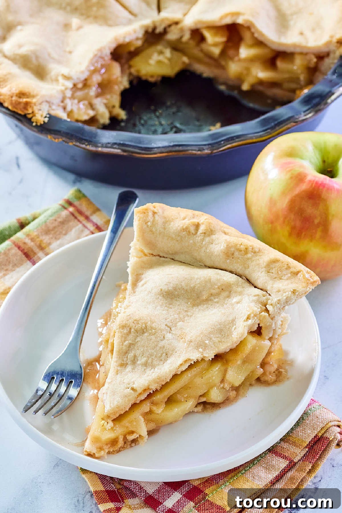 A close-up, top-down view of a generous slice of deep dish apple pie on a small dessert plate with a fork, invitingly ready to be eaten.