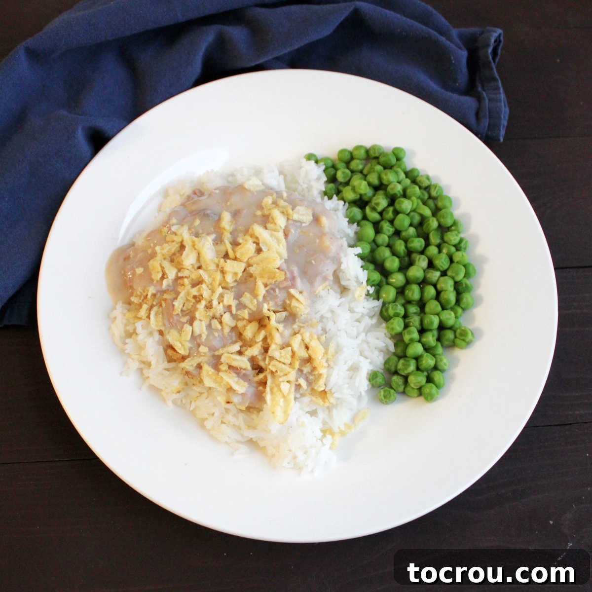 Mimi's Signature Tuna Bake 2 A dinner plate featuring a generous serving of rice and bright green peas, generously topped with Mimi's creamy tuna casserole mixture and a crispy potato chip crust.