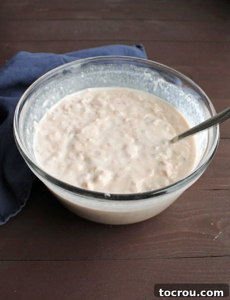 Mimi's Signature Tuna Bake 3 A mixing bowl filled with the creamy base of tuna casserole, combining flaked tuna, condensed cream of mushroom soup, and milk, ready for baking.
