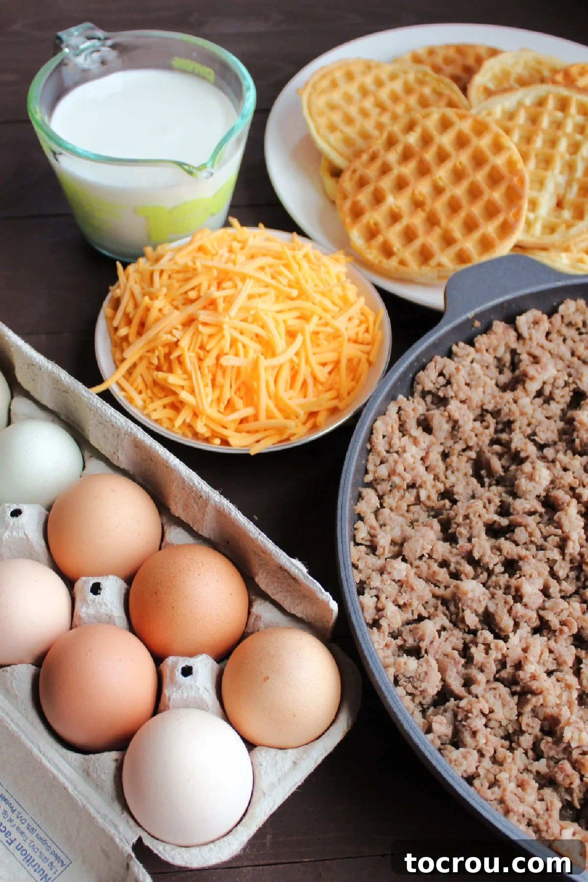 Ingredients for Waffle Breakfast Casserole All ingredients for the waffle sausage breakfast casserole laid out on a kitchen counter, ready for assembly, including frozen waffles, sausage, cheese, eggs, and milk.