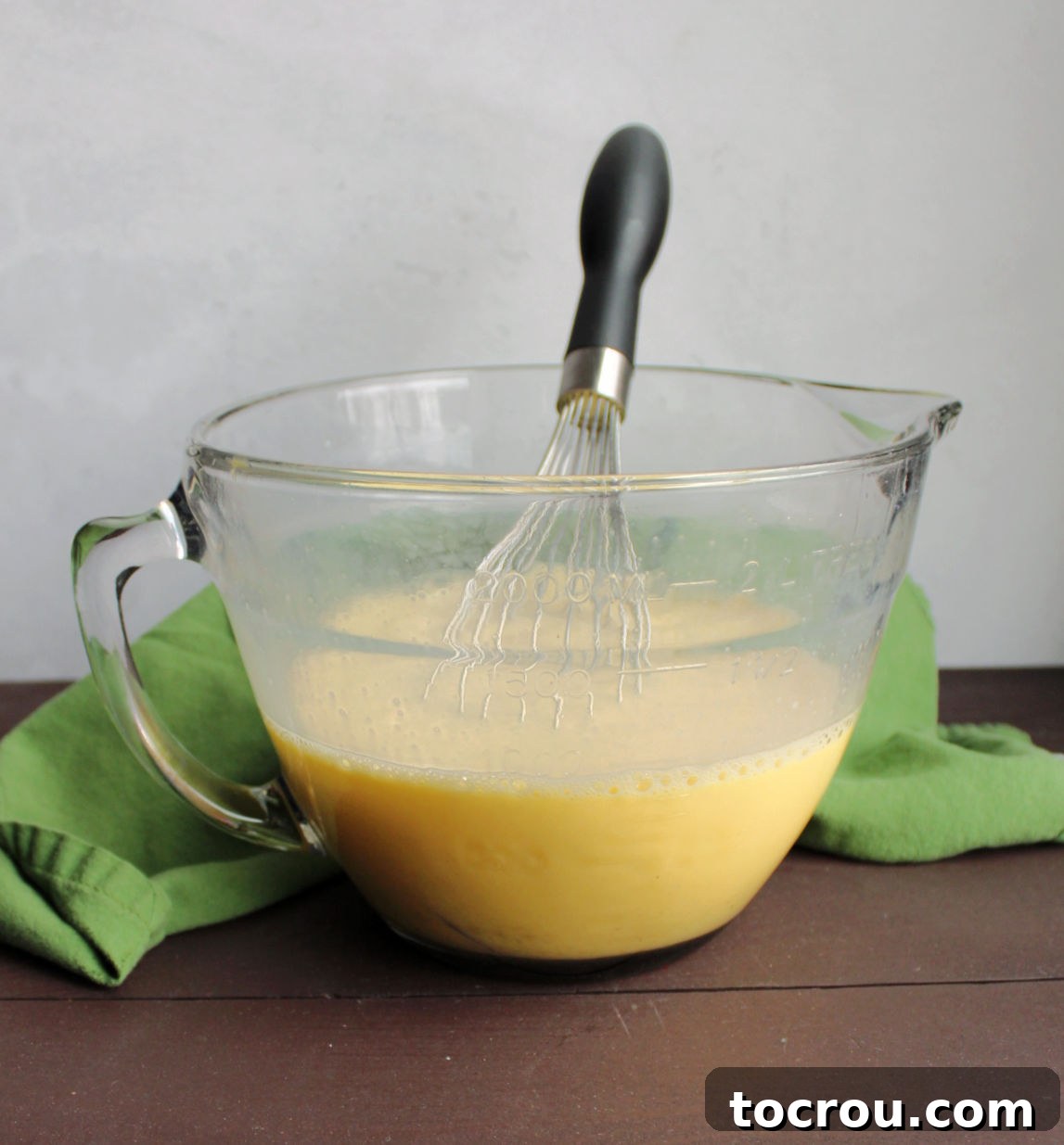 Whisked Egg and Milk Mixture A glass batter bowl filled with whisked eggs and milk, with a whisk resting inside, showing the creamy egg mixture.