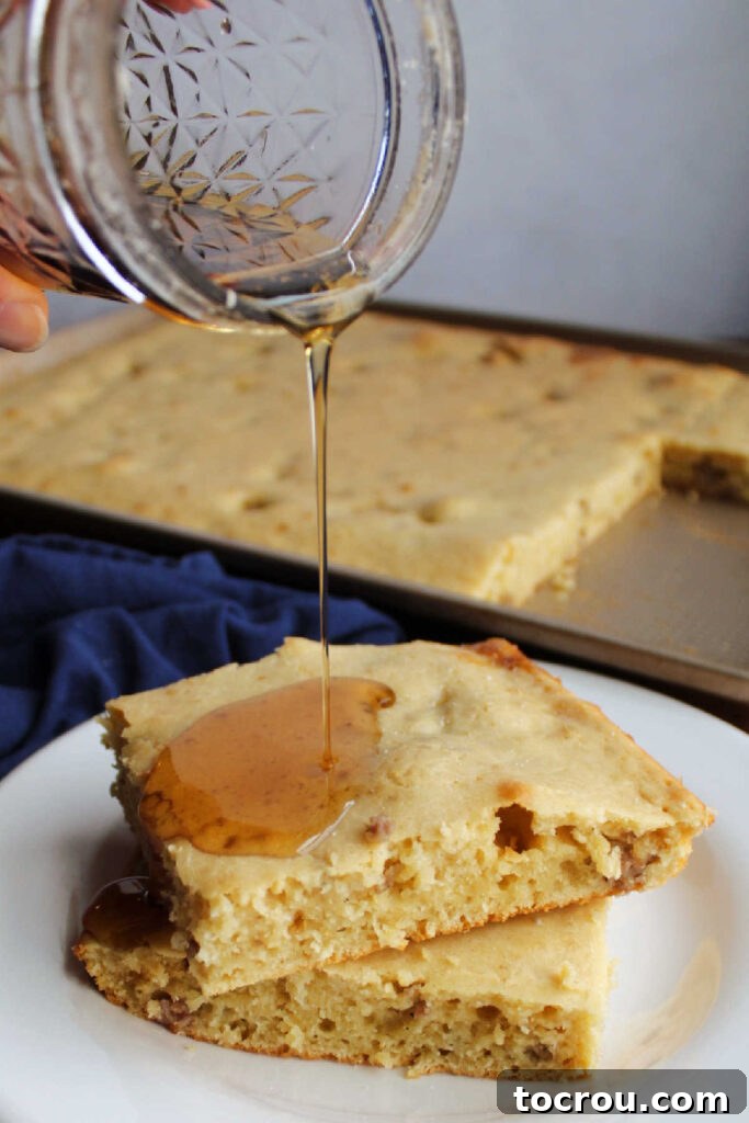 jar of maple syrup being poured over stack of pancake slices on a white plate.