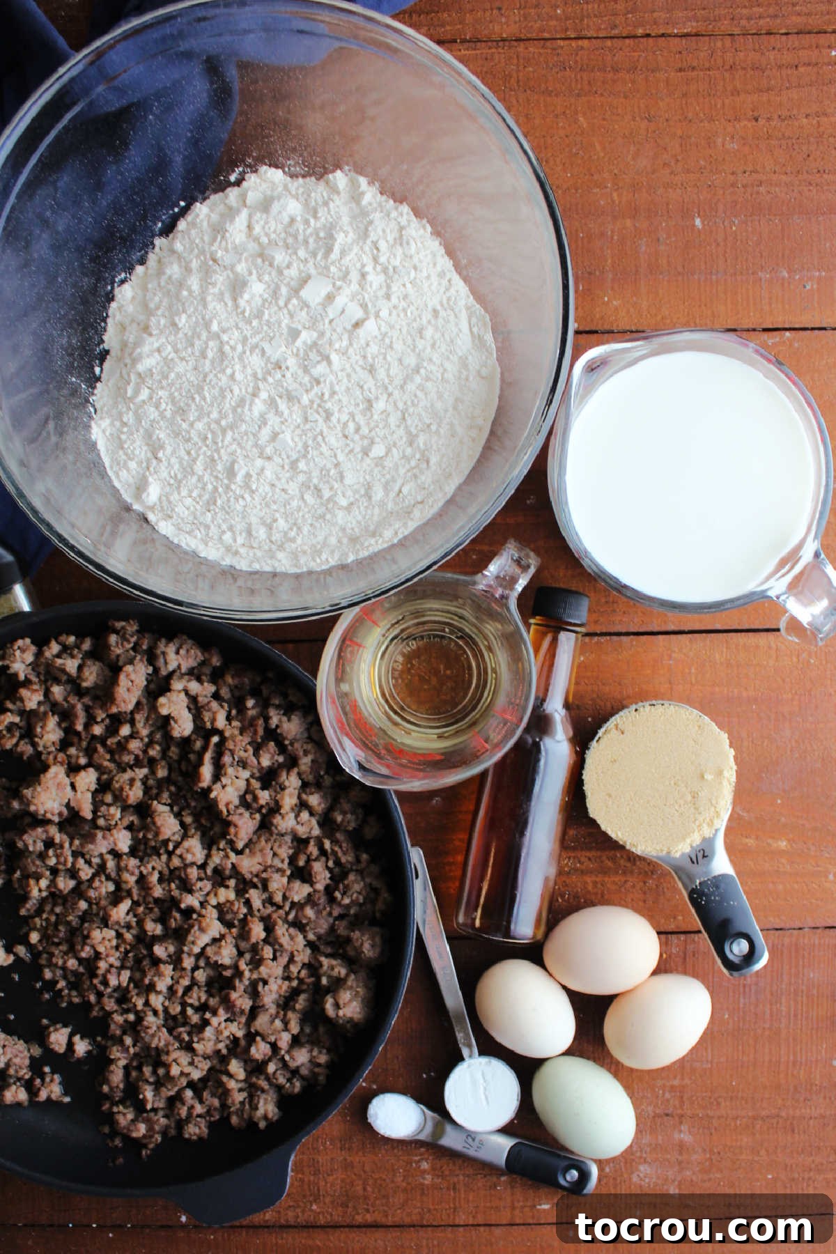 Ingredients including flour, milk, brown sugar, oil, eggs, baking powder, salt and sausage ready to be made into sausage sheet pan pancake batter.
