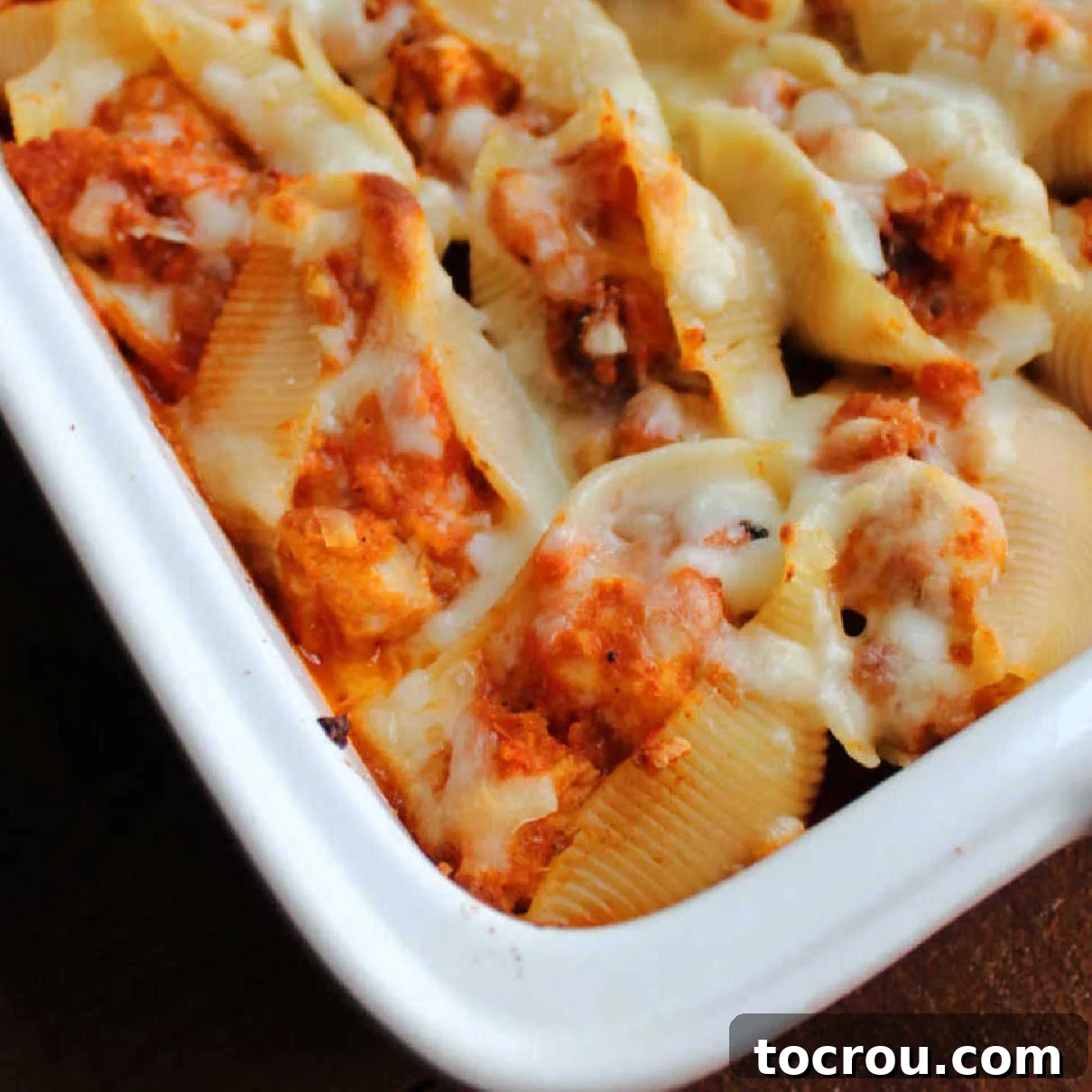 Close up on the corner of a pan of stuffed shells filled with chicken, tomato sauce and cheese, fresh out of the oven.
