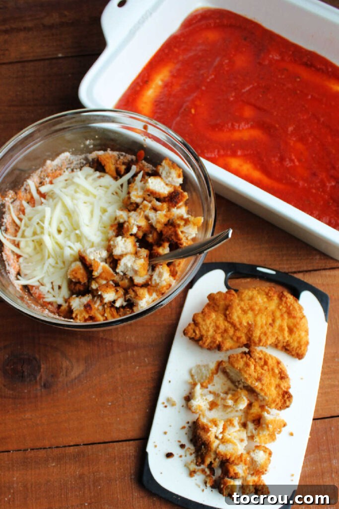 Chopping cooked breaded chicken tenders and placing them in a bowl with sauce and cheese.