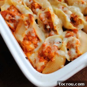 Close up on the corner of a pan of stuffed shells filled with chicken, tomato sauce and cheese.