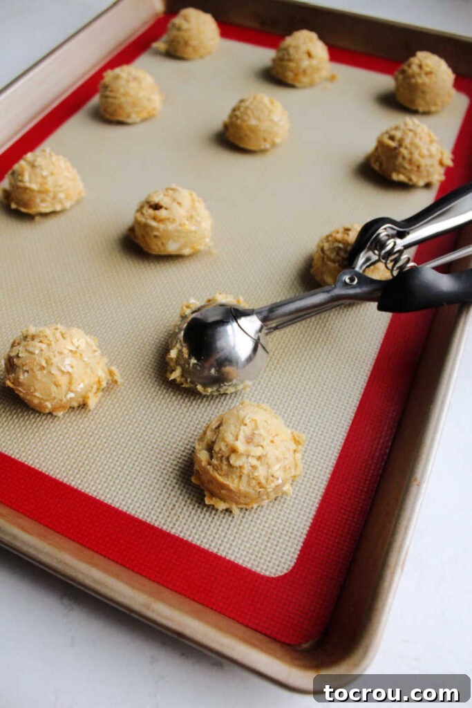 Small, perfectly scooped balls of cookie dough arranged neatly on a silicone mat-lined baking sheet, prepared for baking.