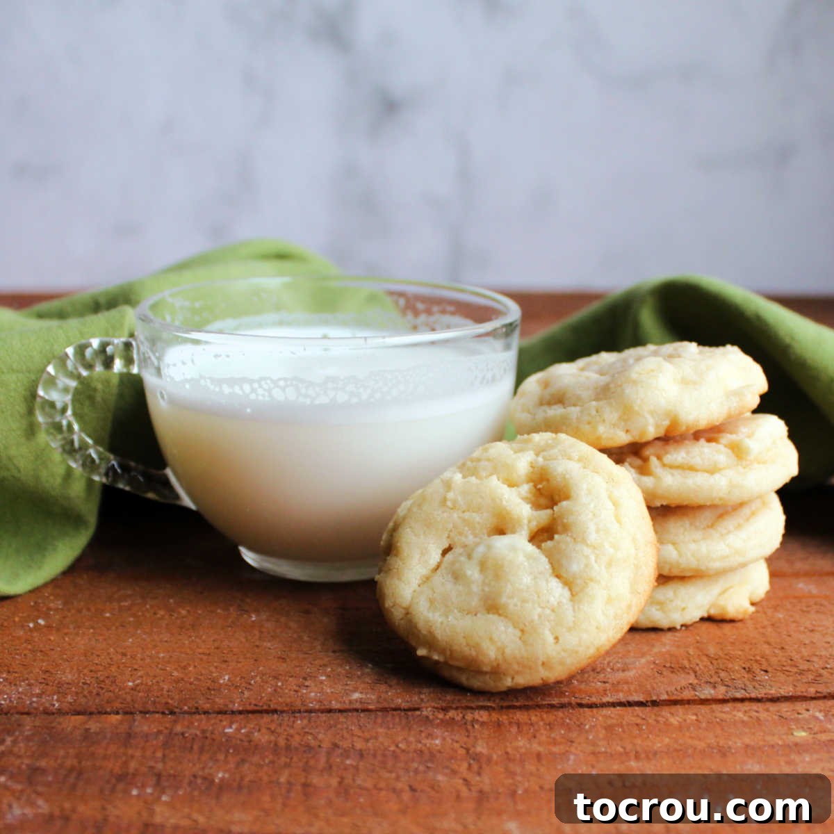 Stack of white hot chocolate cookies next to a small glass mug of white hot chocolate, creating a cozy winter scene.