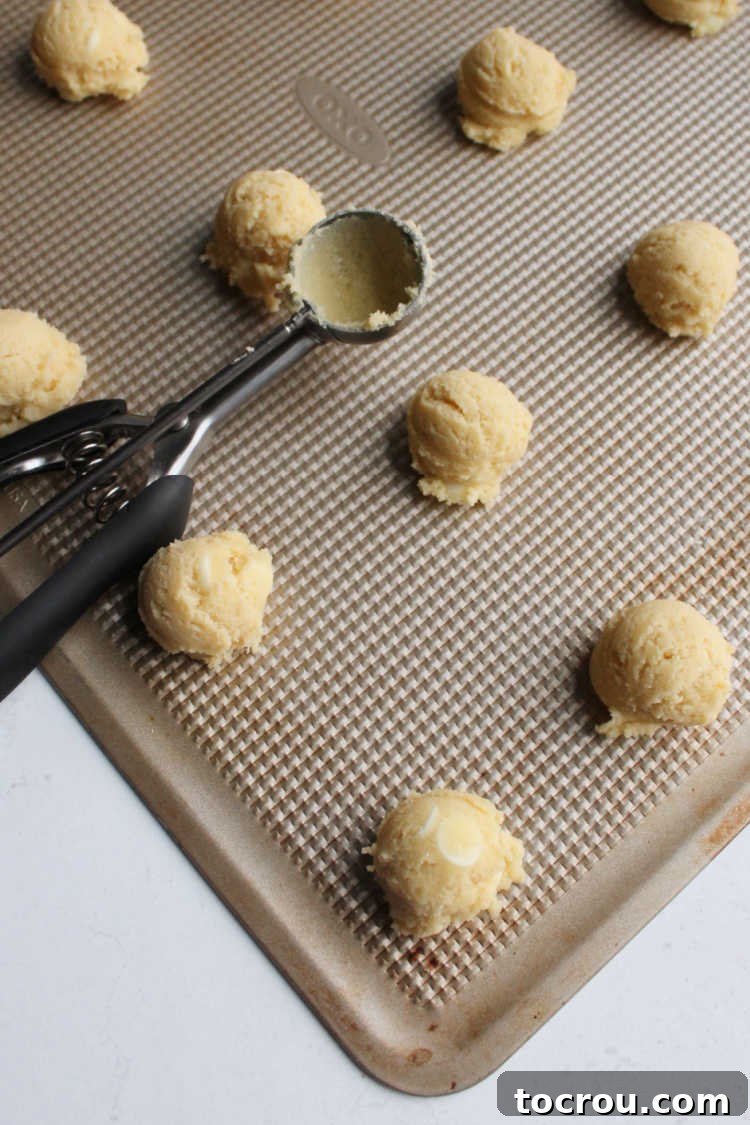 Perfectly scooped balls of white hot chocolate mix cookie dough on a baking tray, ready for the oven.