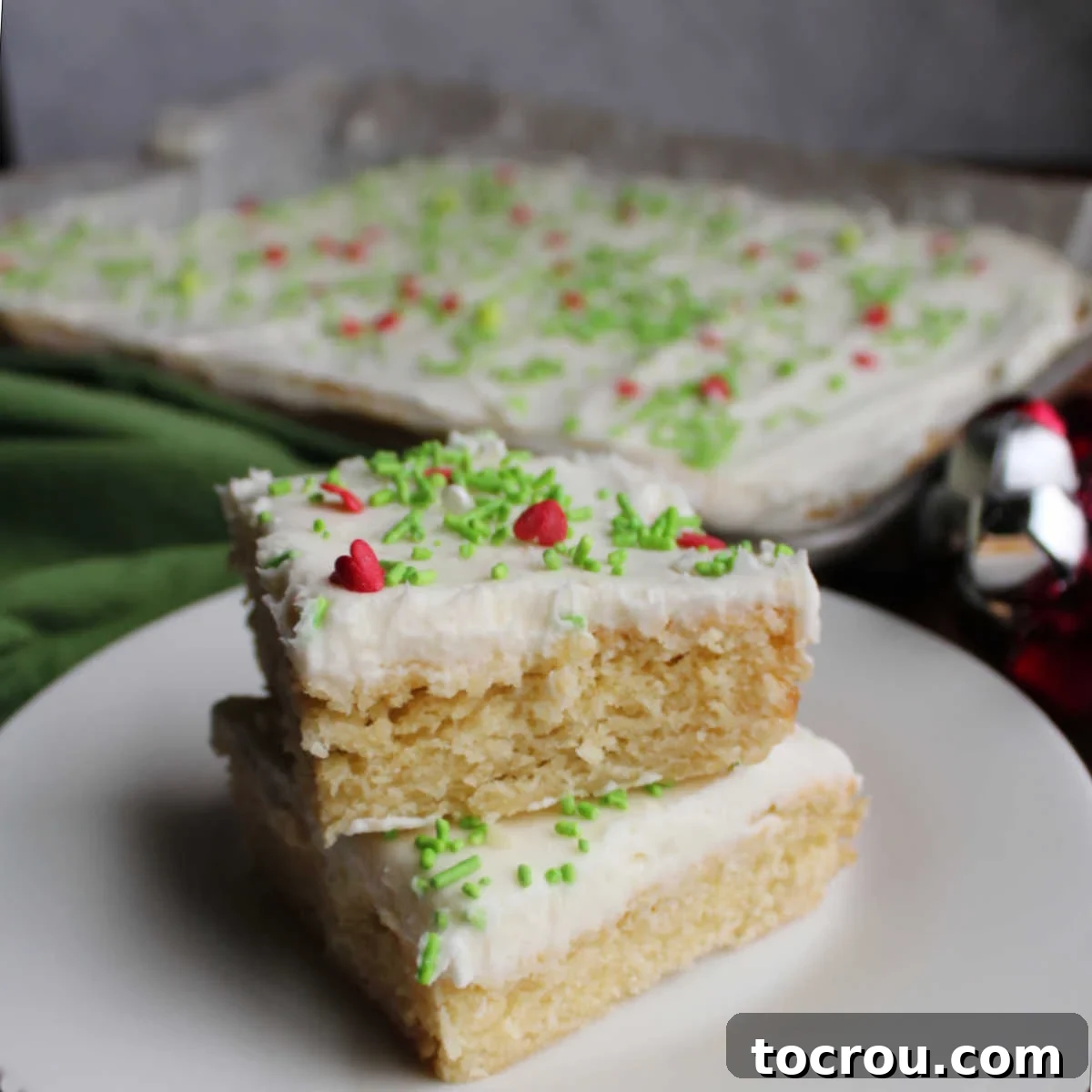 Two frosted sugar cookie bars, topped with white frosting and vibrant sprinkles, stacked on a plate.