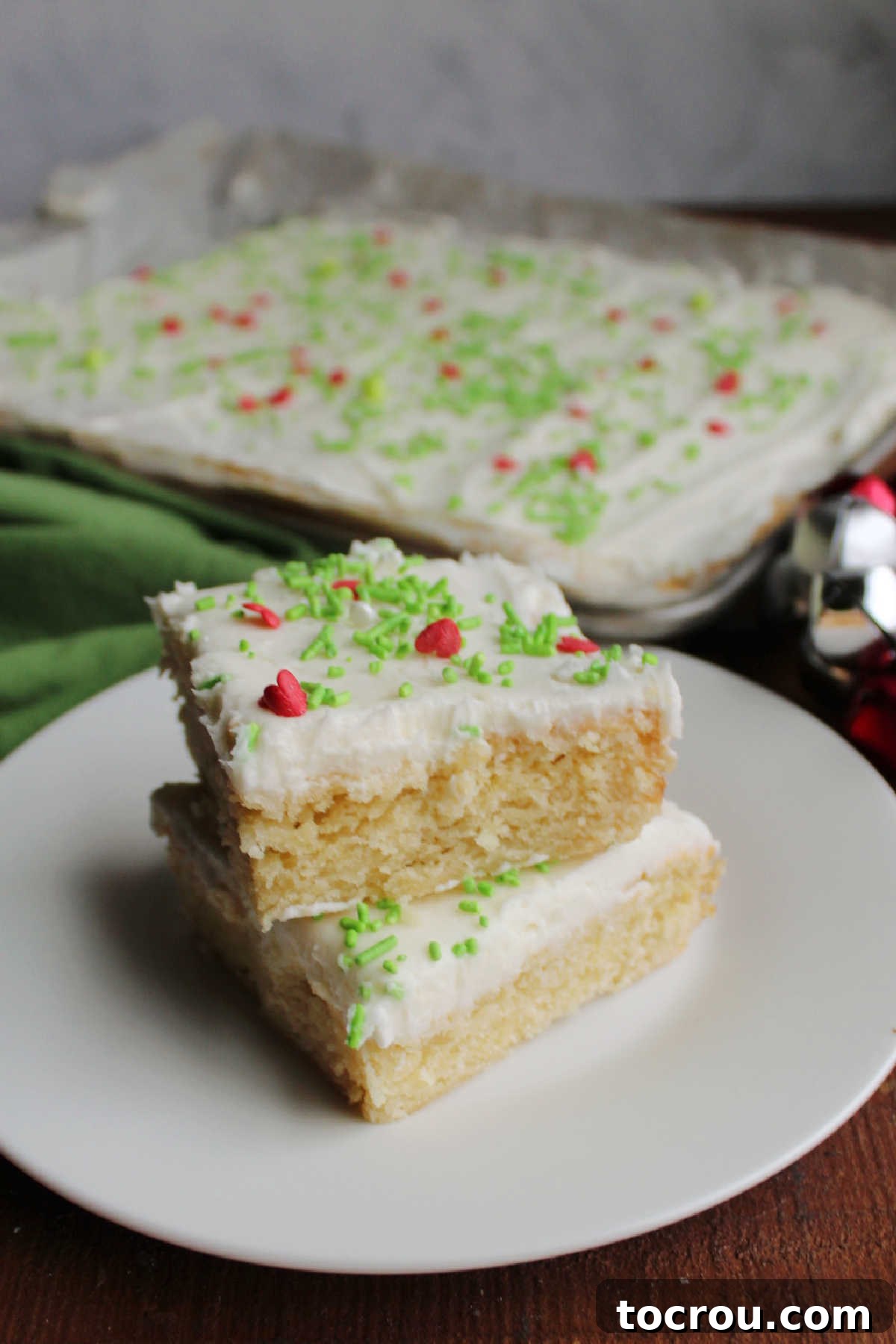 Plate filled with neatly cut squares of soft sugar cookie bars, each topped with creamy vanilla frosting.