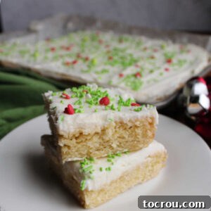Plate with two frosted sugar cookie bars topped with white frosting and sprinkles stacked on top of each other.