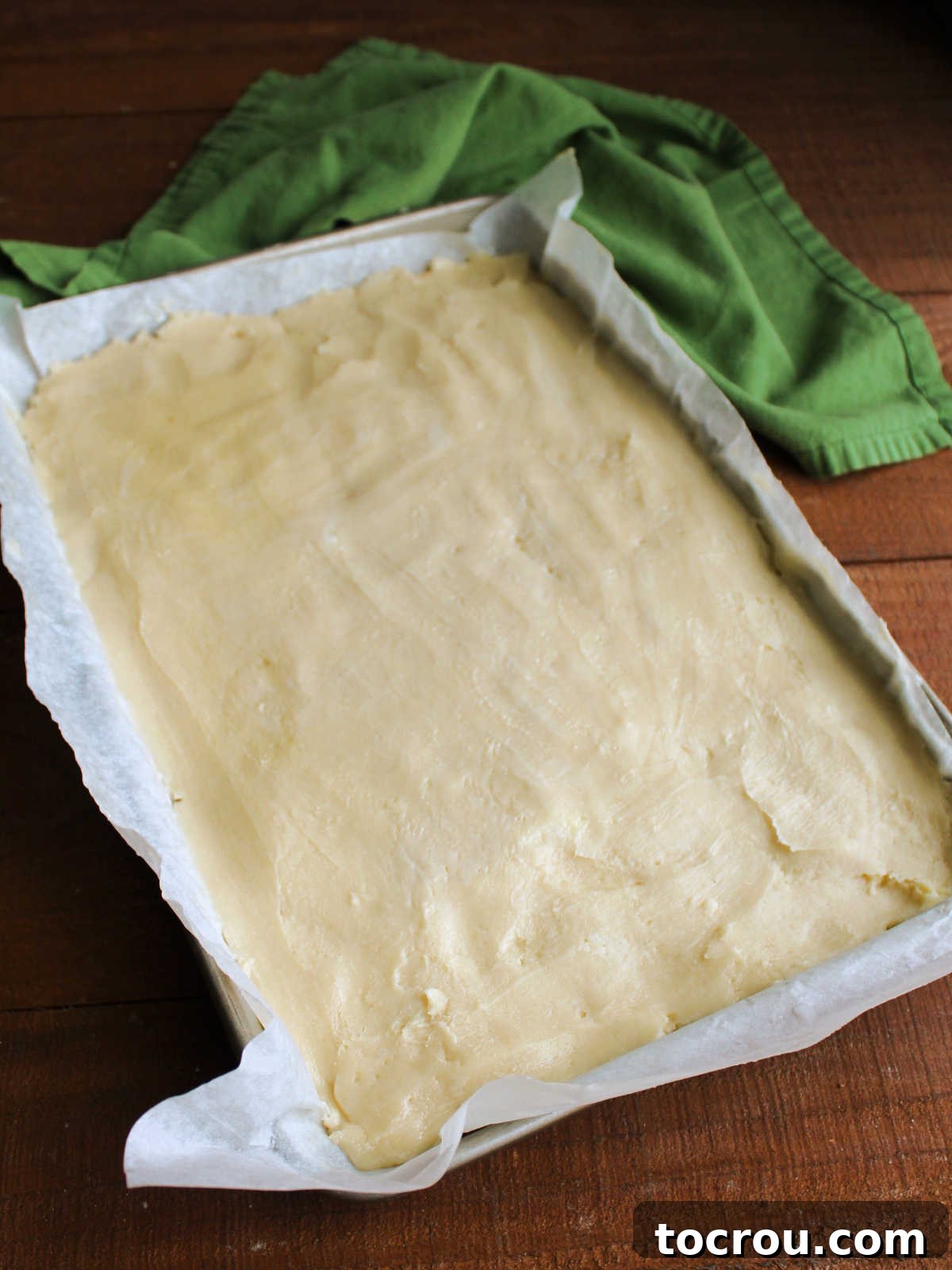 Sugar cookie dough evenly pressed into a parchment paper-lined bar pan, ready for baking.
