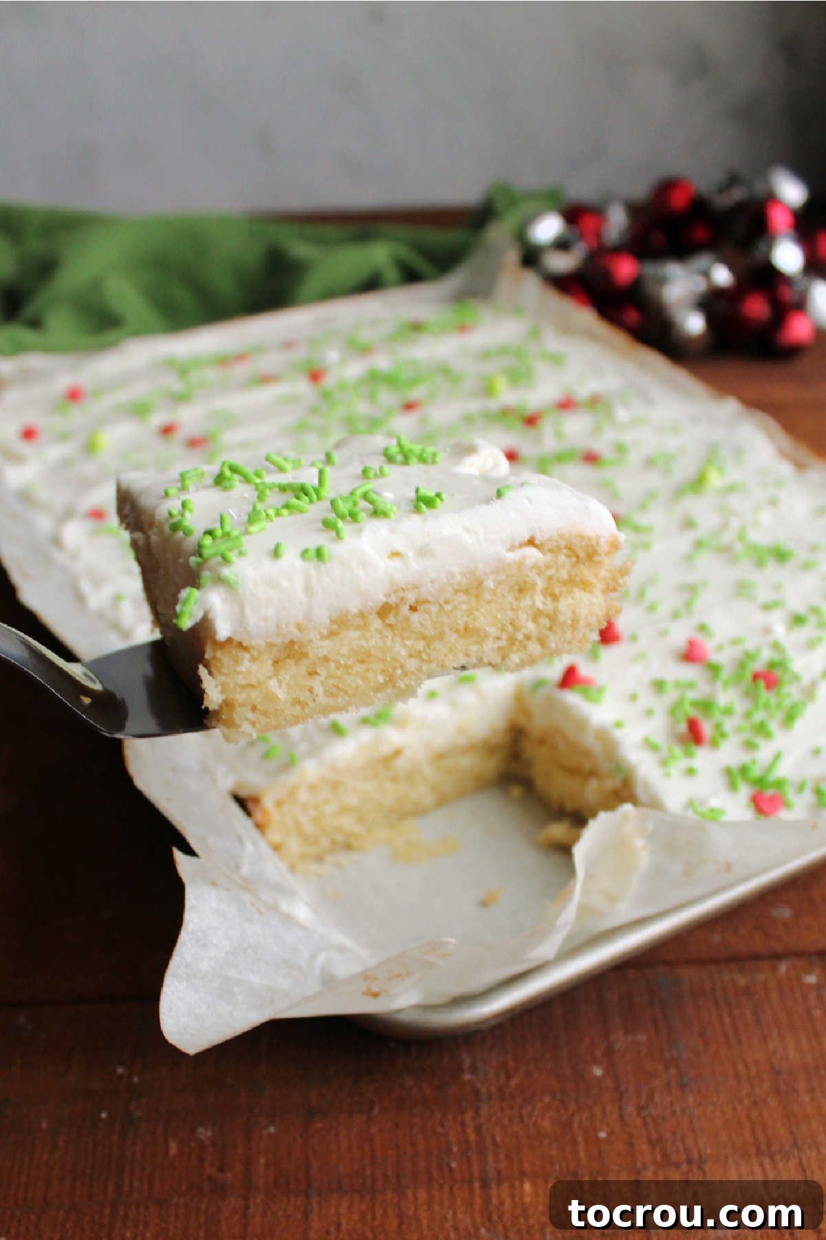 Spatula lifting a soft sugar cookie bar topped with fluffy vanilla buttercream and colorful sprinkles, showcasing its tender texture.