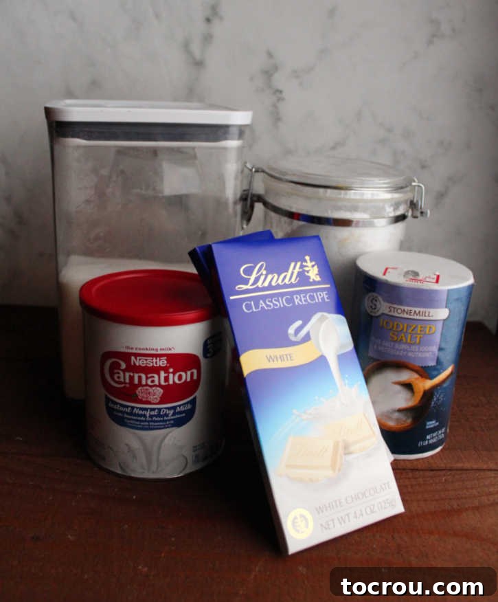 Assorted ingredients for white hot chocolate mix, including white chocolate pieces, various sugars, salt, and powdered milk, laid out on a clean surface ready for preparation.