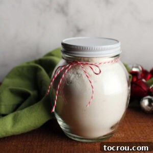 A glass jar filled with the homemade white hot chocolate mix, beautifully tied with a bow, indicating it's ready to be given as a thoughtful gift.