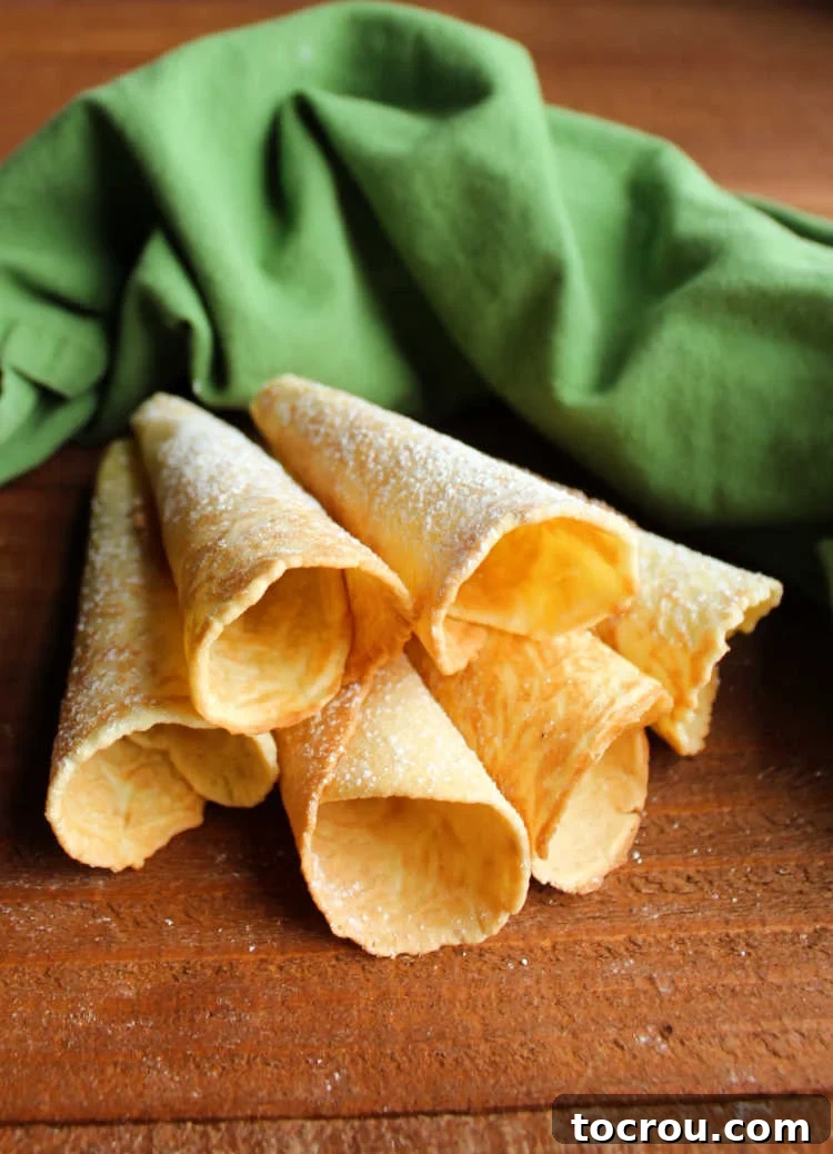 Golden krumkake horns, lightly dusted with powdered sugar, a perfect balance of crispness and sweetness.