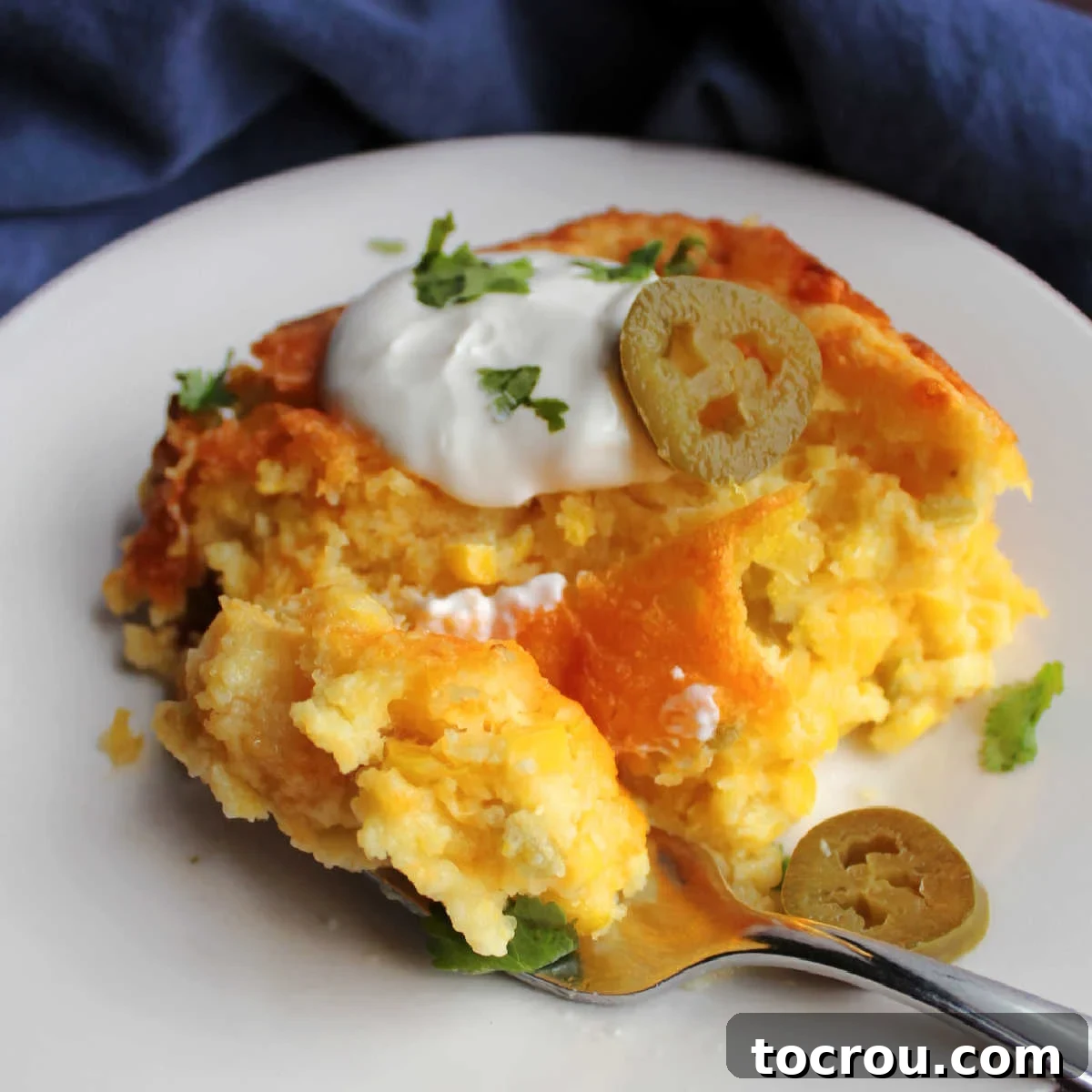 Cheesy Corn Casserole with Green Chiles piece of chili cheese corn pudding topped with sour cream, cilantro and pickled jalapenos.
