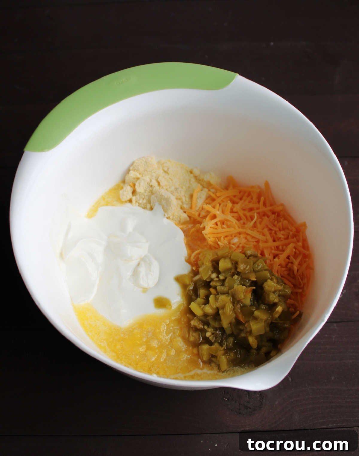 Ingredients for Cheesy Green Chile Corn Casserole bowl full of corn pudding ingredients with green chiles, cheddar cheese, corn, sour cream, corn muffin mix, melted butter and more.