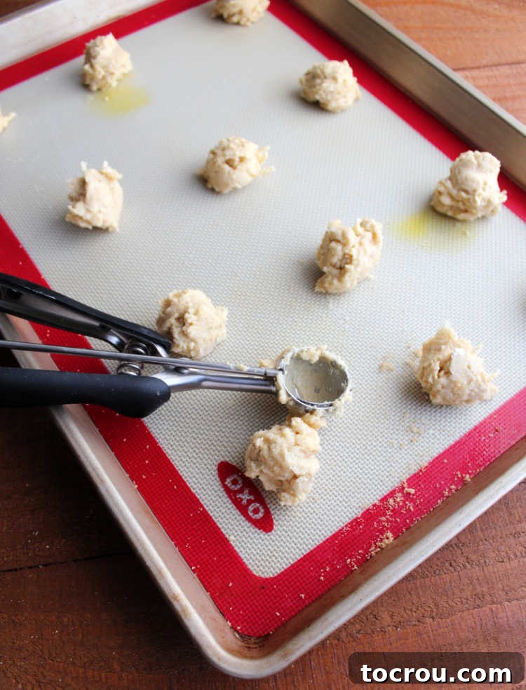 scooping small scoops of cuppa cookie dough onto silicone mat lined baking tray.