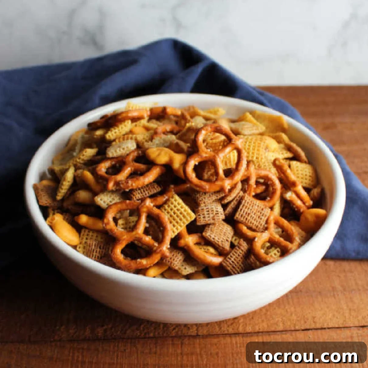 Perfectly golden and crunchy Chex mix, a savory delight for any occasion, especially cherished during the holidays. A large bowl of golden-brown classic Chex mix, featuring a delicious blend of cereals, crunchy pretzels, and savory peanuts, ready to be enjoyed.