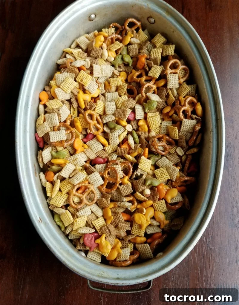 Homemade Chex mix ingredients in a roasting pan, prepped for oven baking. A large, sturdy roasting pan filled with an unbaked mixture of Chex cereals, pretzels, and nuts, coated in seasonings and ready to be placed in the oven.