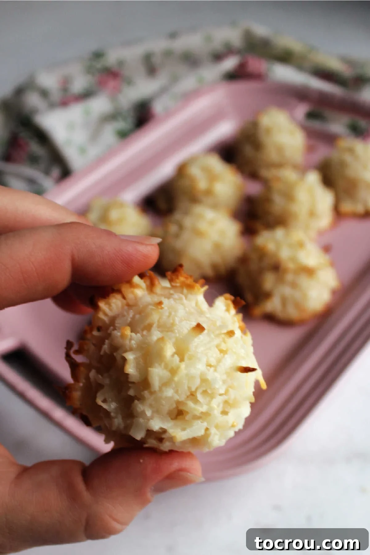 Irresistible Condensed Milk Coconut Bites 7 Hand holding coconut macaroon with platter of cookies in the background.
