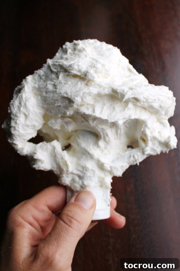 A stand mixer's paddle attachment generously coated with fluffy, pristine white American buttercream frosting.