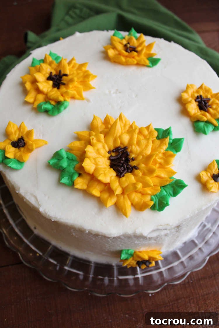 A beautiful layer cake frosted in smooth white buttercream, topped with charming, easy-to-pipe frosting sunflowers.