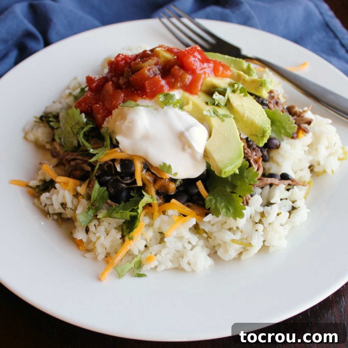 A vibrant burrito bowl featuring fluffy rice topped with tender salsa chicken, creamy avocado, a dollop of sour cream, fresh salsa, and a sprinkle of cilantro.