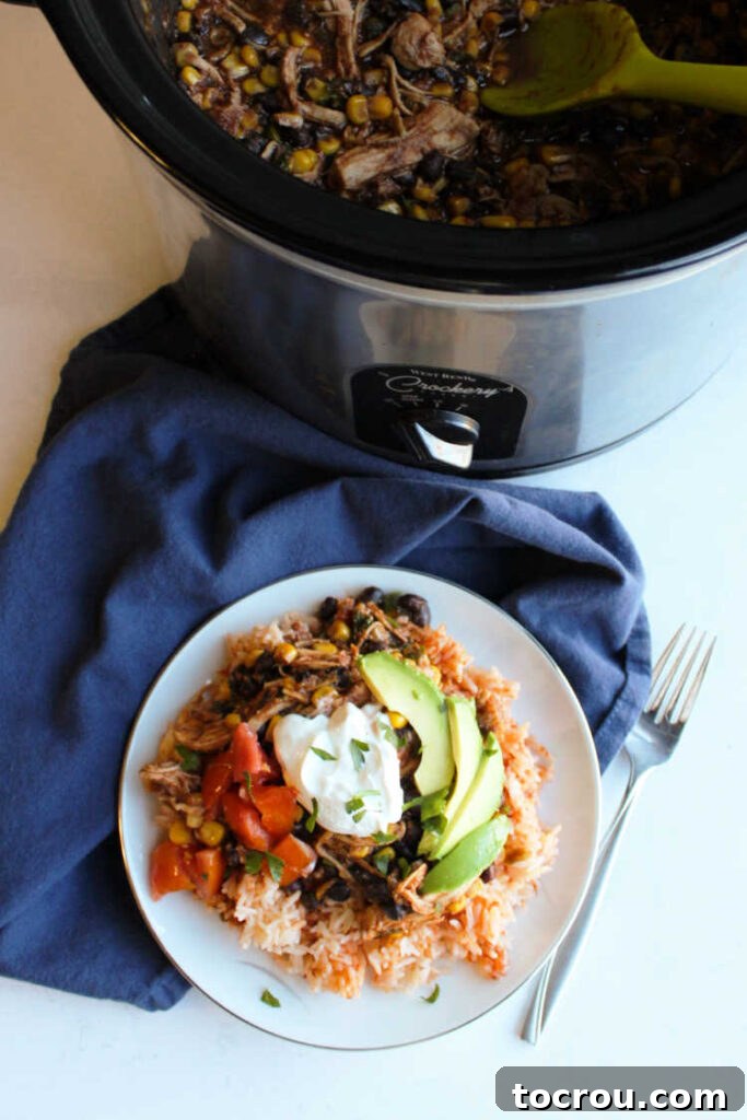 A slow cooker full of delicious salsa chicken sits beside a prepared burrito bowl, showcasing the versatility of the dish.