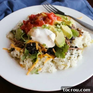 A delicious burrito bowl consisting of fluffy rice topped with flavorful salsa chicken, creamy avocado, a dollop of sour cream, fresh salsa, and other savory toppings.