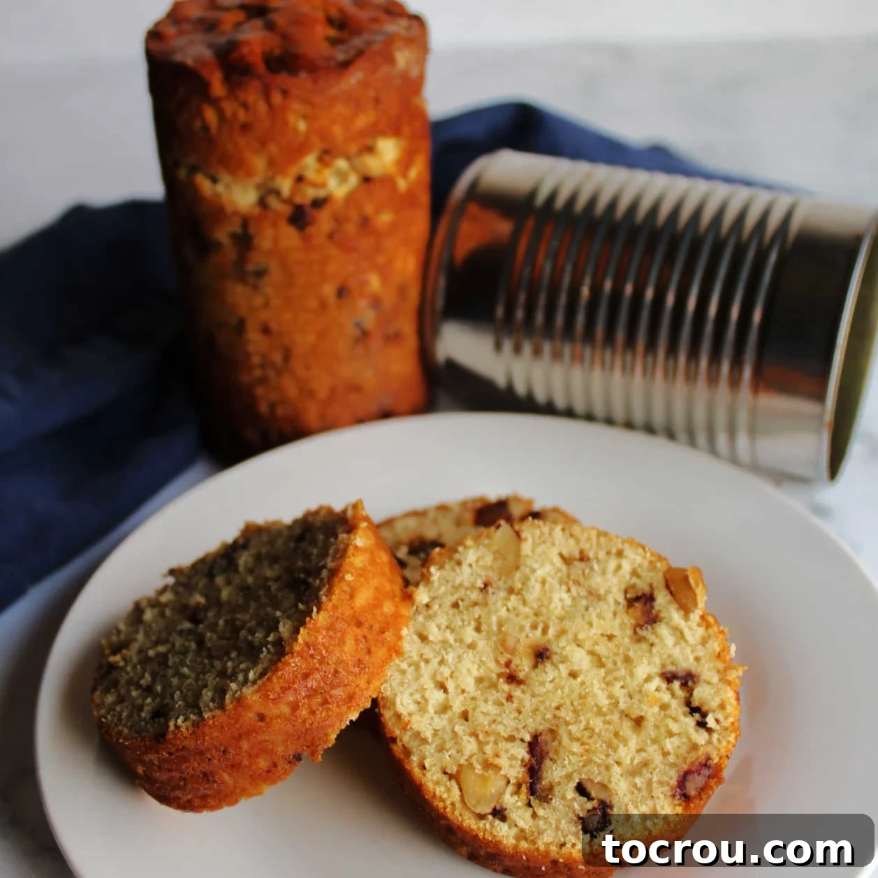 Round slices of date nut loaf on a plate with a tin can and a full loaf in the background, showcasing its delightful texture and form.
