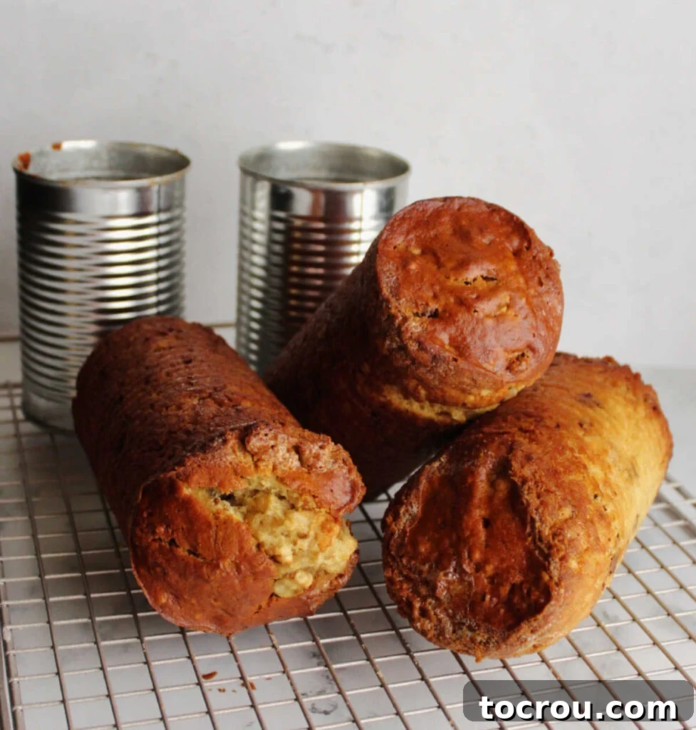 Freshly baked can-shaped date nut bread cooling on a wire rack, with empty tin cans visible in the background.
