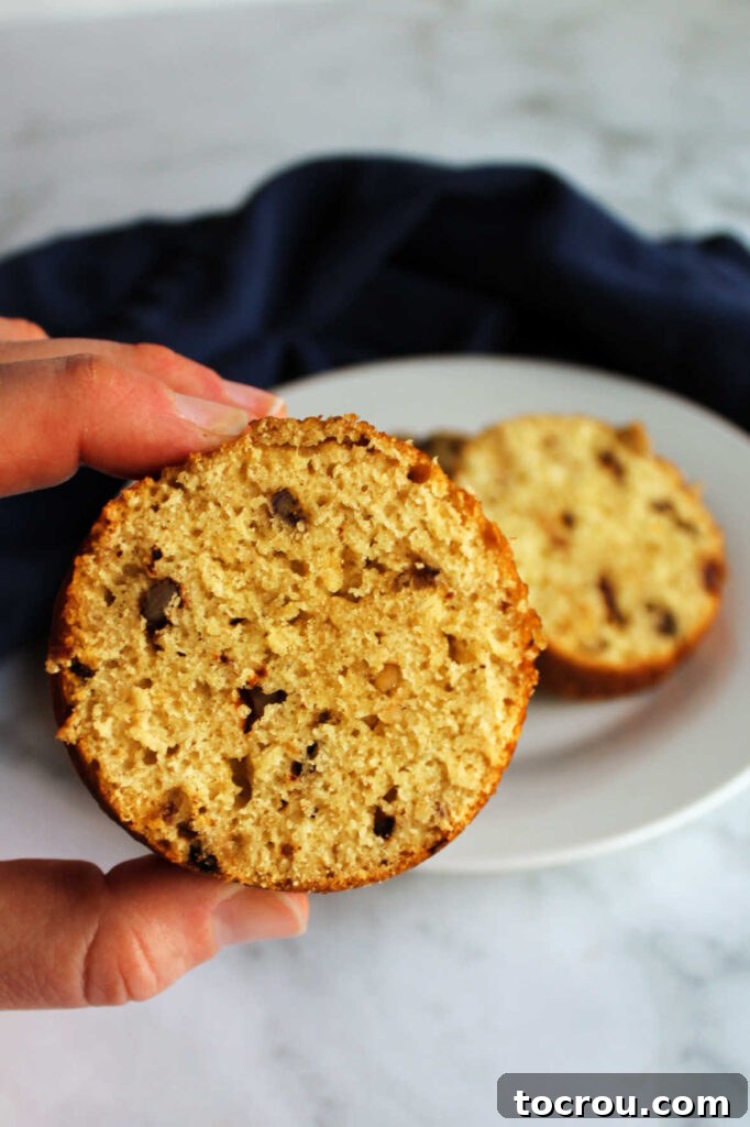A hand holding a perfectly round slice of date walnut bread, illustrating its unique can-baked shape and inviting texture.