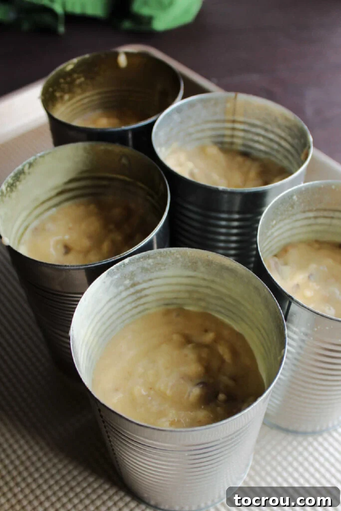 Greased tin cans filled with date walnut loaf batter, neatly arranged and ready for the oven.