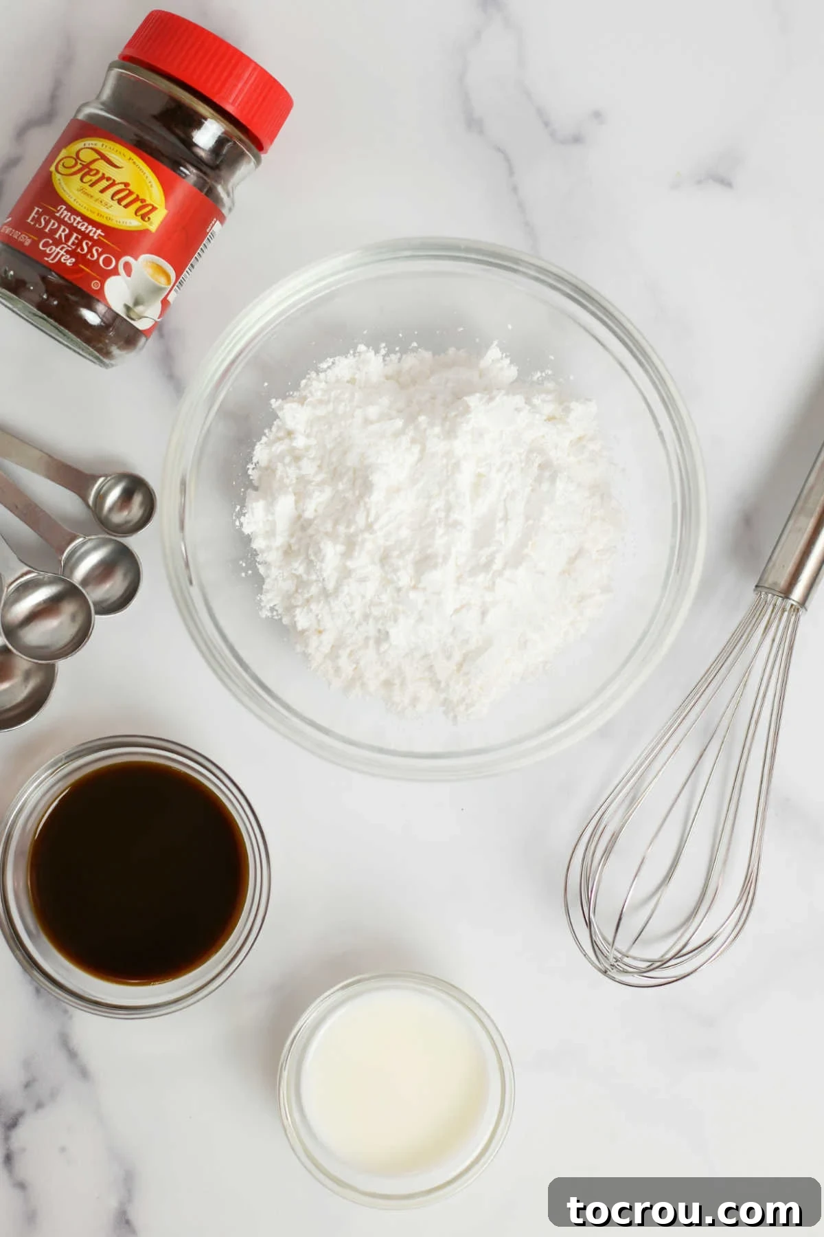 Ingredients for espresso glaze, including powdered sugar, milk, vanilla extract, and instant espresso, arranged with a whisk and measuring spoons.